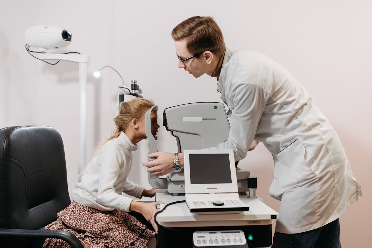 Young girl undergoing eye examination with optometrist using medical equipment in a clinic.